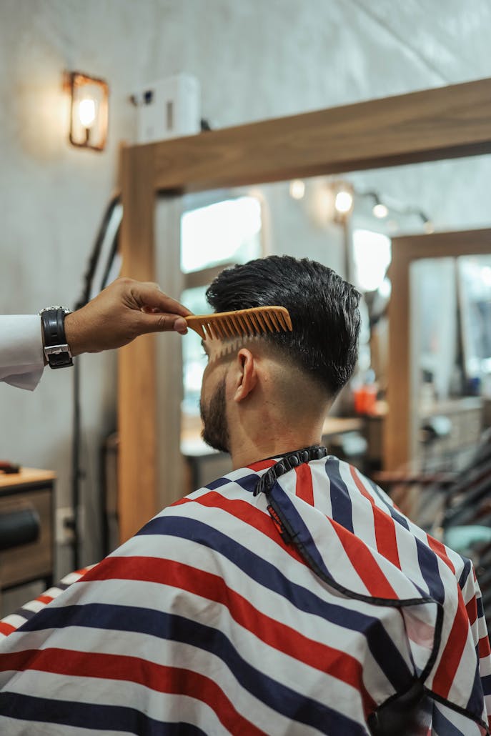 Barber styling a man's hair with a comb in a contemporary salon setting.